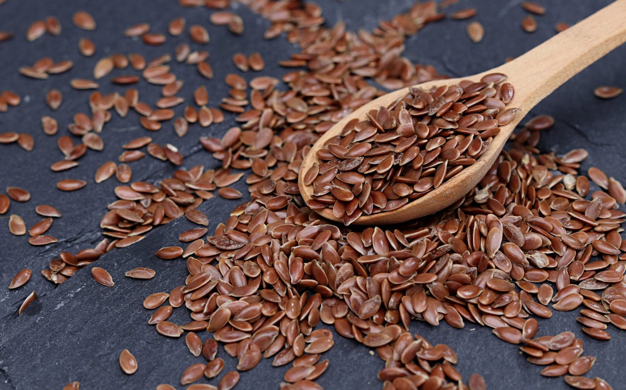 Close-up of brown flax seeds scattered with wooden spoon on slate.
